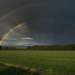 A beautiful rainbow stretches across the sky, illuminating the serene countryside with its vivid colors.