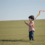 A child gazing up at their soaring kite, representing the beautiful connection to nature and carefree play.