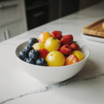 A vibrant bowl of assorted fresh fruit on a kitchen counter, showcasing natural colors and textures.