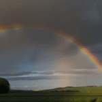 The calm of the countryside is enhanced by a stunning rainbow, arching across the sky in a display of nature's artistry.