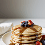 Mouthwatering pancake stack drenched in syrup and adorned with juicy berries, an irresistible morning delight.
