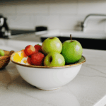 A bowl of fresh fruits, arranged to highlight their natural colors and textures on a counter.
