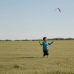 A vibrant kite soaring high, guided by a child's enthusiastic hands against the backdrop of a lush green field.