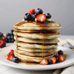 Close-up of golden pancakes with a generous serving of syrup and vibrant berries, ideal for brunch lovers.