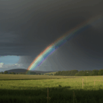 A majestic rainbow stretches over a peaceful countryside, painting the sky with its vibrant colors and enchanting charm.