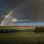A picturesque rainbow spans the sky over a tranquil countryside, creating a breathtaking view of vibrant serenity.