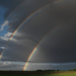 In the peaceful countryside, a rainbow casts its colorful arch, offering a moment of tranquility and natural beauty.