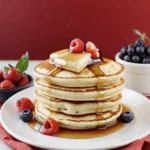 A stack of fluffy pancakes drizzled with syrup and topped with fresh berries, perfect for a delicious breakfast treat.