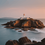 A picturesque lighthouse illuminated by the setting sun on a rugged coast.