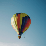 A vibrant hot air balloon soaring through a clear blue sky, showcasing its colorful patterns.