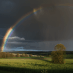 A colorful rainbow spans across a tranquil countryside sky, offering a breathtaking view of nature's majestic beauty.